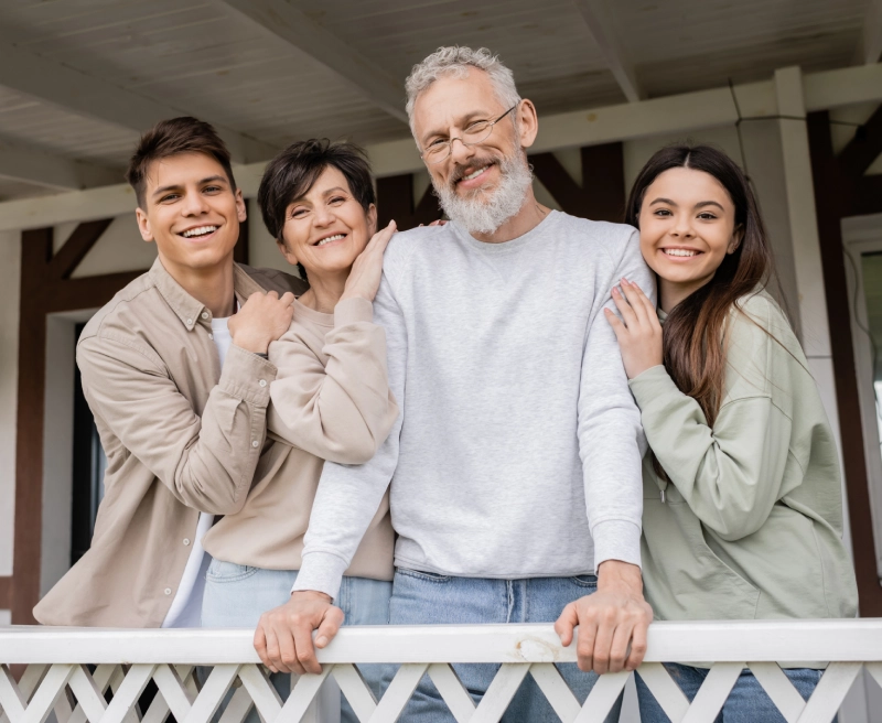 Smiling family of four standing on a porch railing, showing warmth and togetherness outdoors