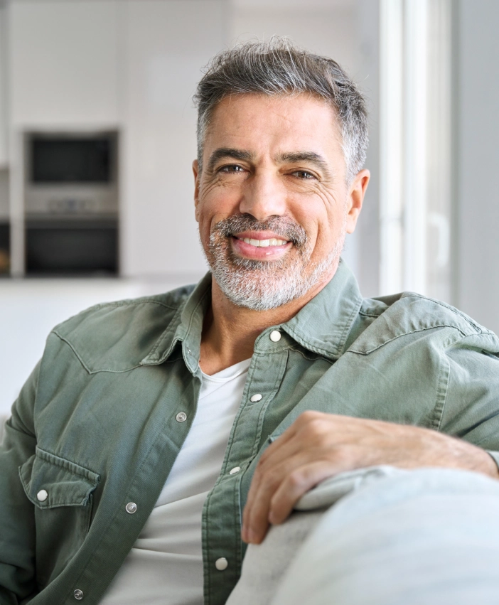 Smiling man sitting comfortably indoors, exuding confidence, warmth, and a relaxed demeanor