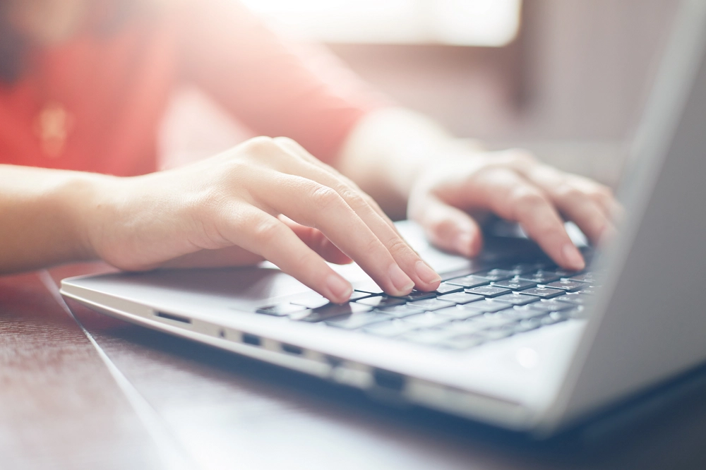 Close-up of a person’s hands typing on a laptop keyboard in soft natural light