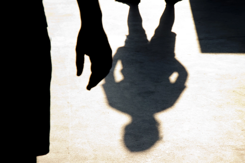 Shadow of a person with hands on hips cast on the ground, with another person’s silhouette partially visible in the foreground