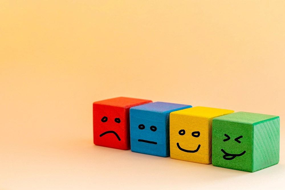 Colorful wooden blocks with different facial expressions representing a range of emotions on a yellow background