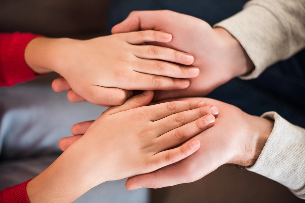 Close-up of multiple hands stacked together, showing unity, support, and care among family or friends