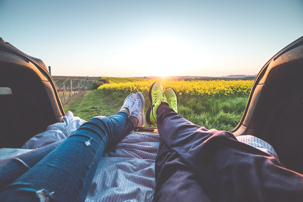 Couple relaxing in the back of a car, watching the sunset over a scenic field of flowers
