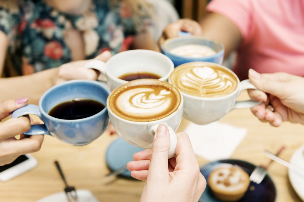 Group of friends clinking coffee mugs together at a café table