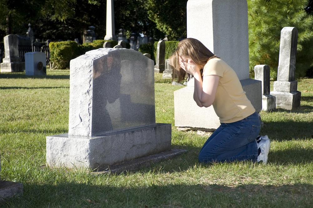 Woman kneeling and crying at a gravestone in a cemetery